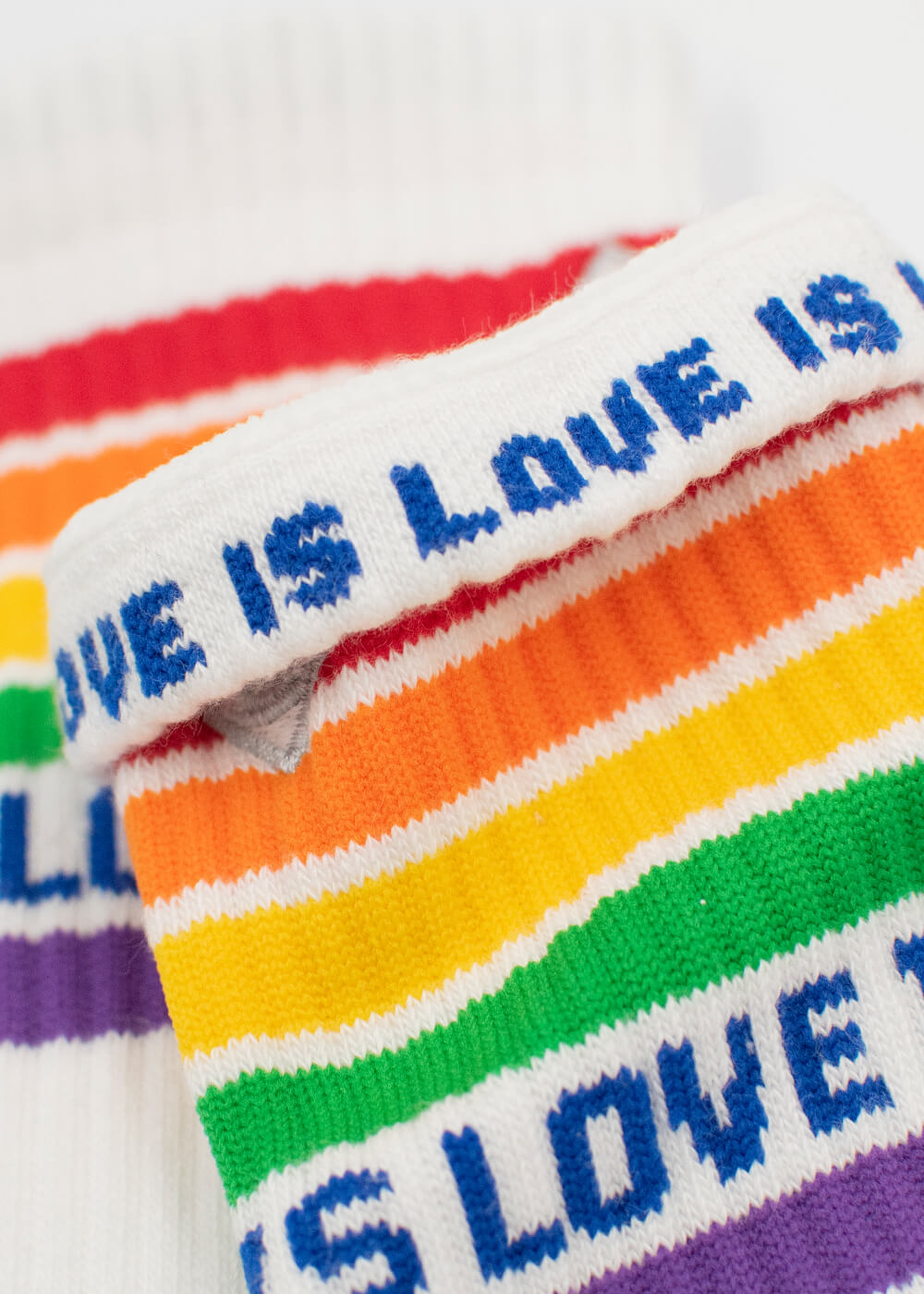 Nahaufnahme der weißen J.Clay Tennissocken mit Regenbogenstreifen und dem blauen Schriftzug LOVE IS LOVE entlang des Bündchens.