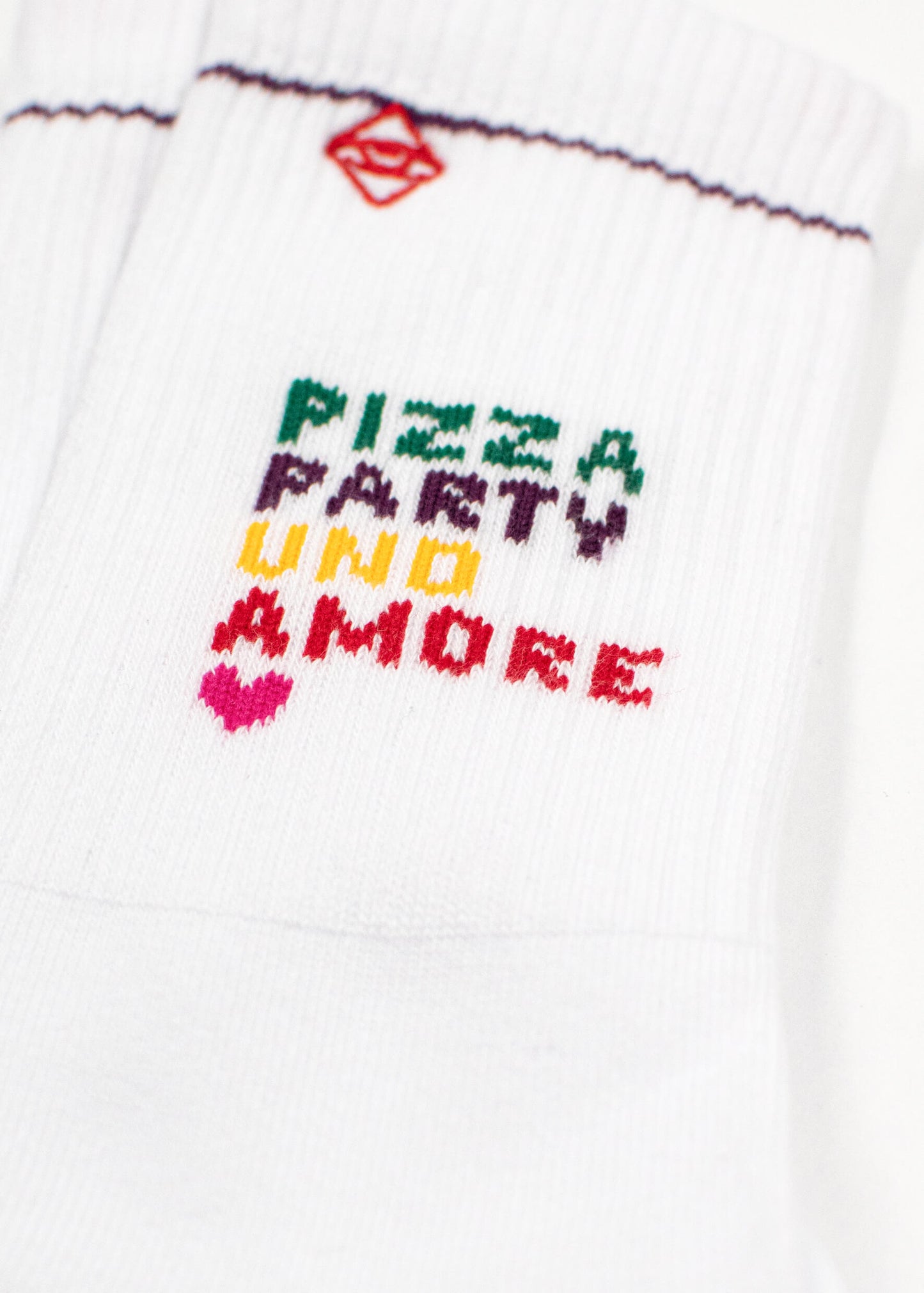 Nahaufnahme von weißen J.Clay-Tennissocken mit gerippter Struktur, buntem gesticktem Text mit der Aufschrift PIZZA PARTY VINO AMORE und einem kleinen roten geometrischen Muster oberhalb des Schriftzugs.