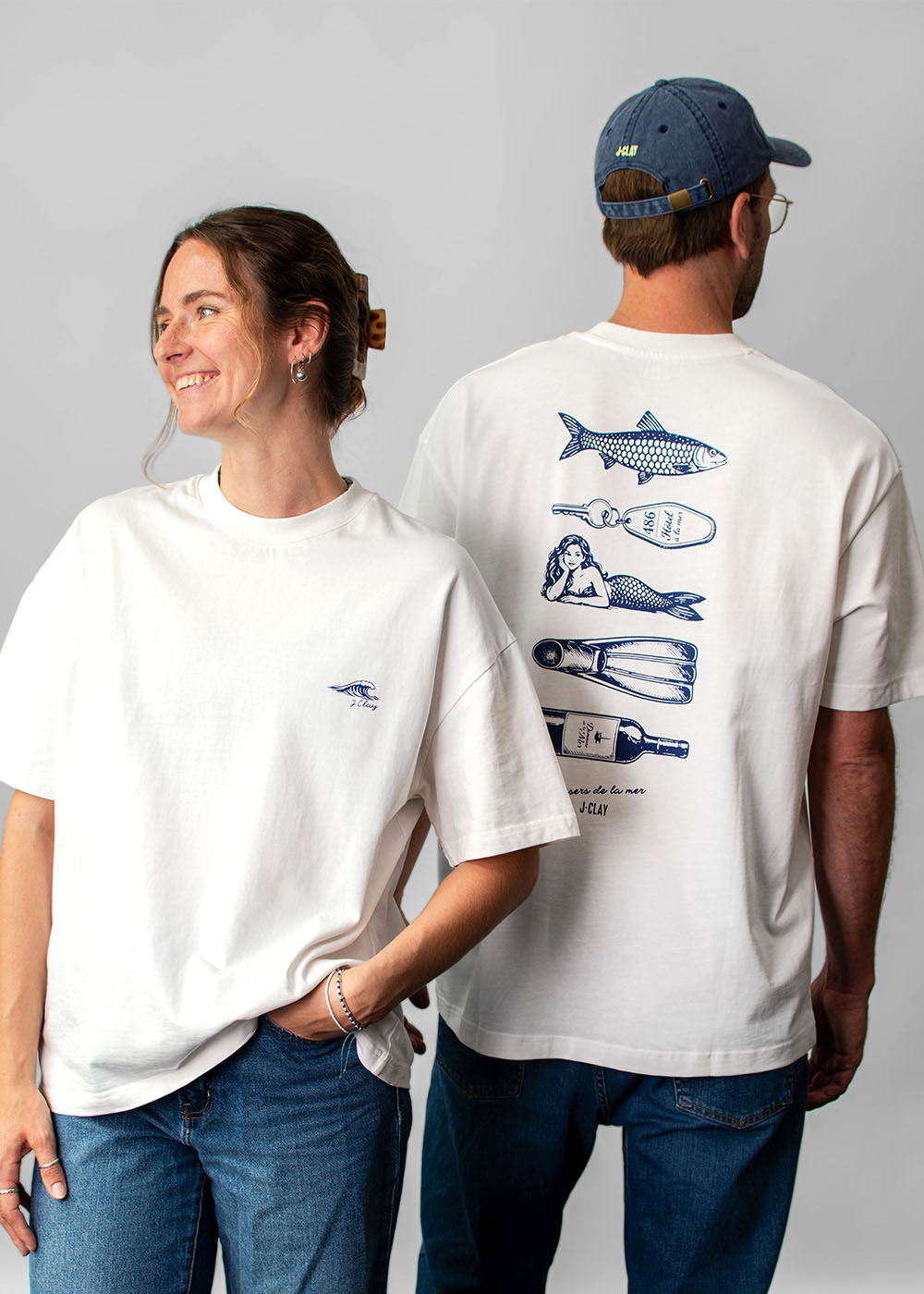 Zwei Personen tragen weiße Unisex-T-Shirts der Marke J.Clay Ocean Kiss, wobei sowohl die Vorder- als auch die Rückseite zu sehen sind.