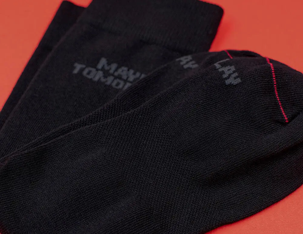 Business Socken für Damen - Ein Paar schwarze Socken mit schwacher grauer Schrift und einem kleinen roten Streifen an der Spitze, die auf einer roten Fläche liegen.