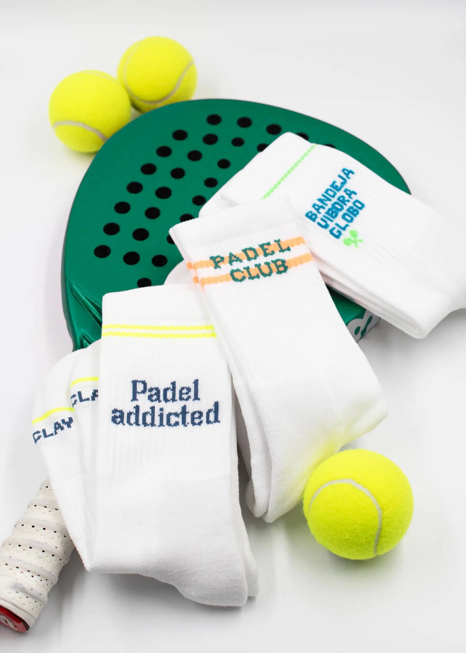 Ein grüner Padel-Schläger, weiße Socken mit Padel-Schriftzug und mehrere gelbe Tennisbälle sind vor einem weißen Hintergrund angeordnet.