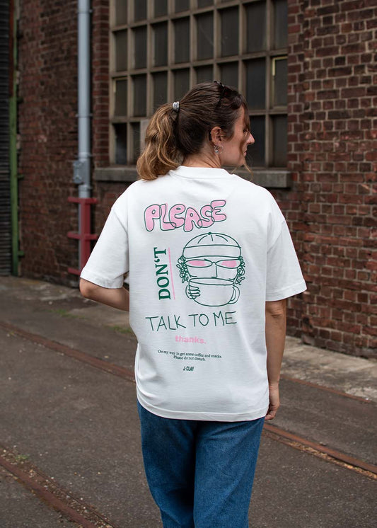 Eine Frau trägt ein „J.Clay Please Don’t“-T-Shirt mit buntem Aufdruck auf der Rückseite und steht draußen.