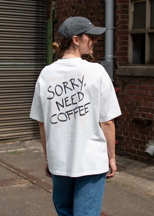 Eine Person in einem „J.Clay Sorry Need Coffee“-T-Shirt steht draußen vor einer Backsteinmauer.