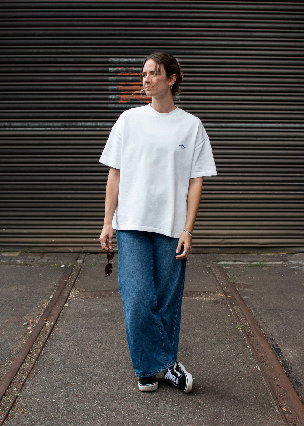 Eine Person in einem „J.Clay Ocean Kiss“-T-Shirt und blauen Jeans steht vor einer Tür aus Wellblech.