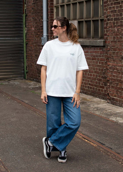 Frau mit Sonnenbrille, „J.Clay Please Don’t“-T-Shirt, blaue Jeans und Turnschuhe, die auf einer Straße steht.
