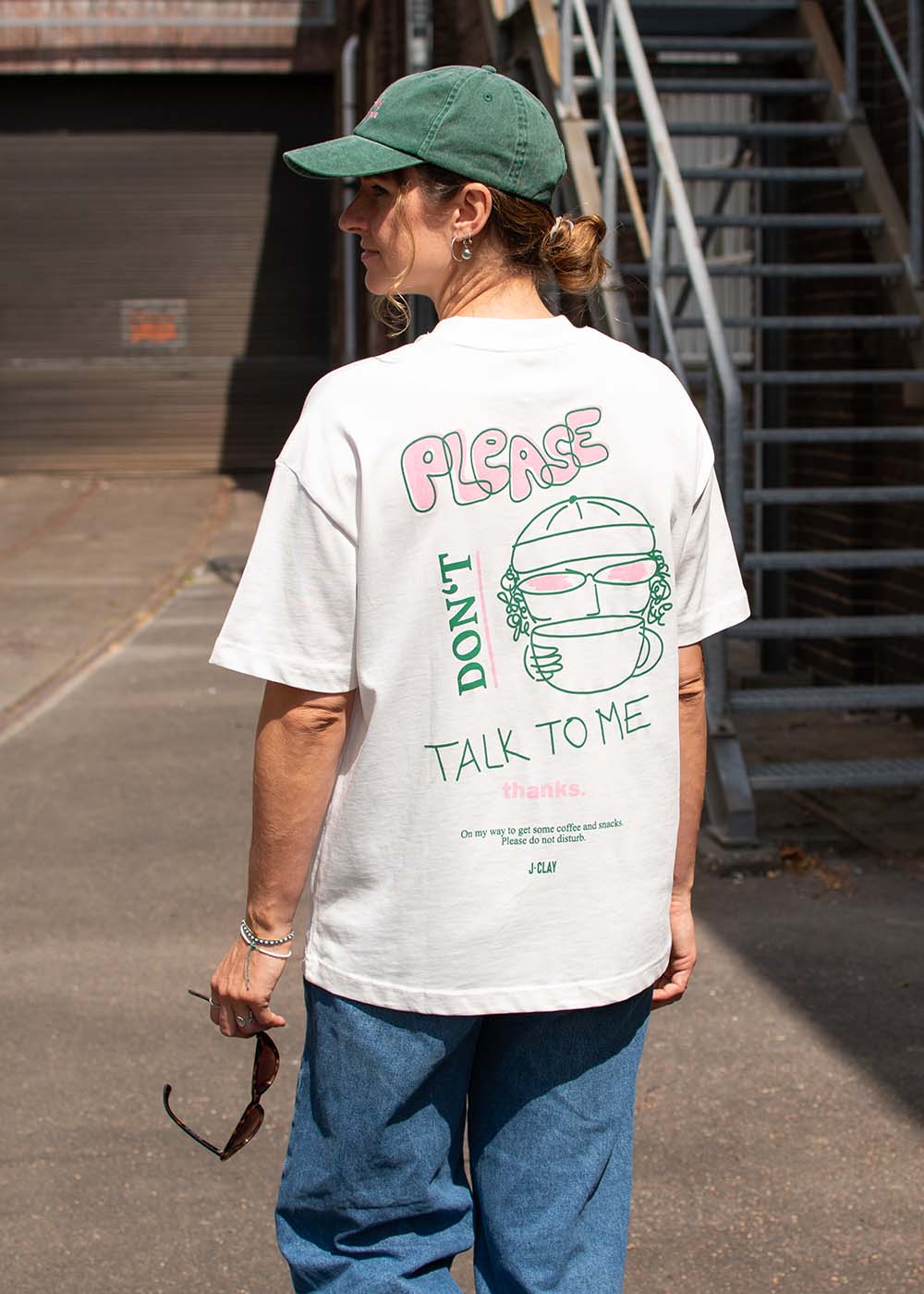 Eine Person in einem T-Shirt mit der Aufschrift „J.Clay Please Don’t“ steht neben der Außentreppe.