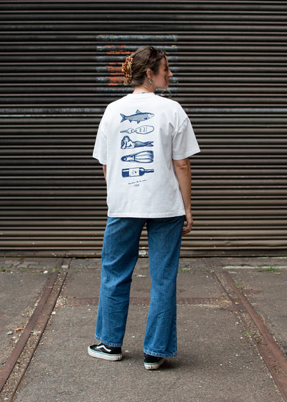 Eine Person in einem „J.Clay Ocean Kiss“-T-Shirt mit blauen Fisch- und Besteckmotiven steht auf einer Straße.
