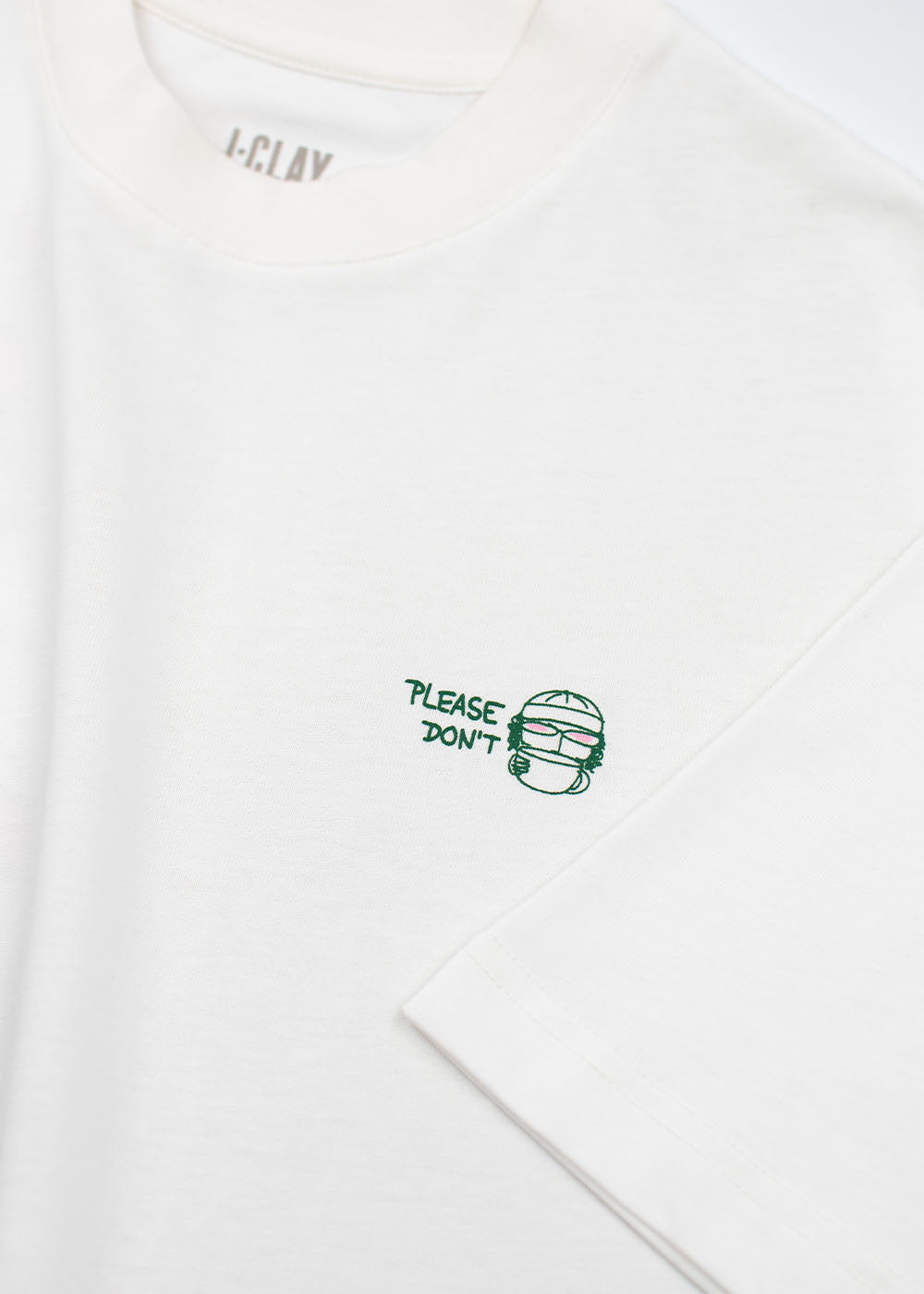 J.Clay „Please Don’t“ – Unisex-T-Shirt in Off-White, Oversize-Passform, mit grünem Schriftzug und Gesichtsillustration.