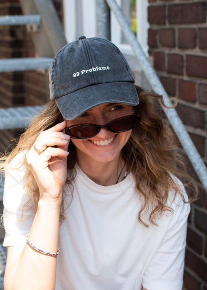 Eine Frau mit Mütze liest „99 Problems“ von J. Clay und schiebt ihre Sonnenbrille hoch, während sie eine Treppe aus Ziegeln und Metall hinaufsteigt.