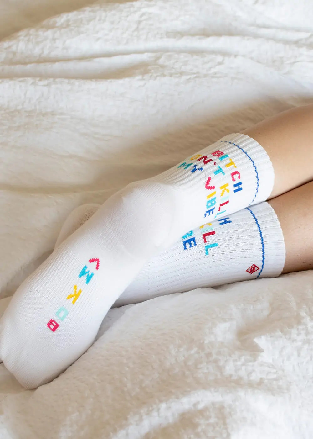 Eine Person mit J.Clay "Bitch don't kill my vibe"-Socken liegt auf einem weißen Bett.