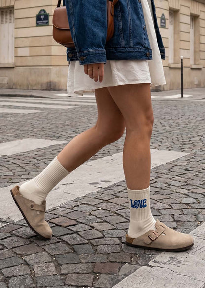 Person in weißem Kleid, Denim-Jacke und J.Clay boho love Socken spaziert.
