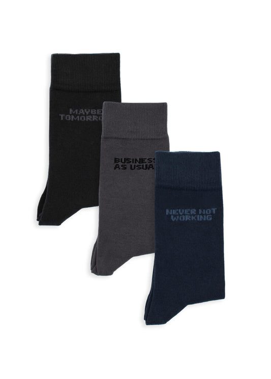 Drei Paar J.Clay Business-Socken in Schwarz, Grau und Marineblau liegen nebeneinander. Auf jedem Paar steht ein Spruch in der Nähe des Bündchens: "MAYBE TOMORROW", "BUSINESS AS USUAL" und "NEVER NOT WORKING".