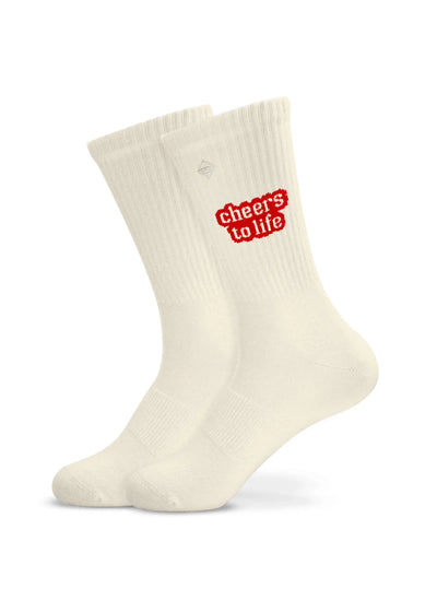 Ein Paar weiße J.Clay "Cheers to life" Tennissocken aus einer Baumwollmischung mit rotem Text in der Nähe des oberen Randes sind auf einem schlichten weißen Hintergrund abgebildet.