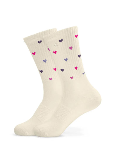 Ein Paar cremefarbene J.Clay Tennissocken mit einem verstreuten Muster aus kleinen roten, rosa, lila und marineblauen Herzen auf weißem Hintergrund.