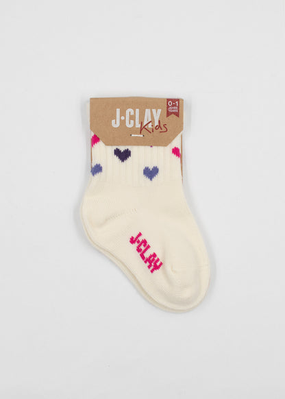 Ein Paar cremefarbene Baby Socken von J.Clay mit blauen, lila und rosa Herzmustern und "J-CLAY" in rosa. Ausgestellt mit einem braunen Etikett mit der Aufschrift "Kinder Socken 0-4 Jahre.