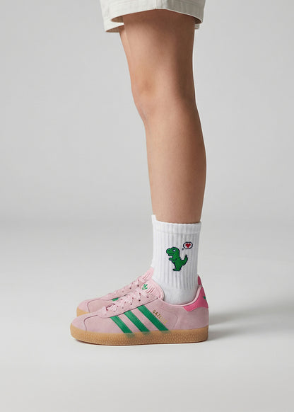 Kind in rosa und grünen Turnschuhen trägt J.Clay Dino Love - Kindersocken mit Cartoon-Dinosaurier-Design.