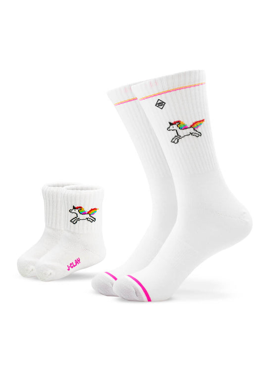 Zwei Paar weiße J.Clay Mini Me Socken - ein Paar für Erwachsene, ein Paar für Kinder - jeweils mit einem bunten Einhorn-Design. Das Paar für Erwachsene hat eine pinke Spitze und einen orangefarbenen Rand, der perfekt zum Partner-Look der Socken passt.