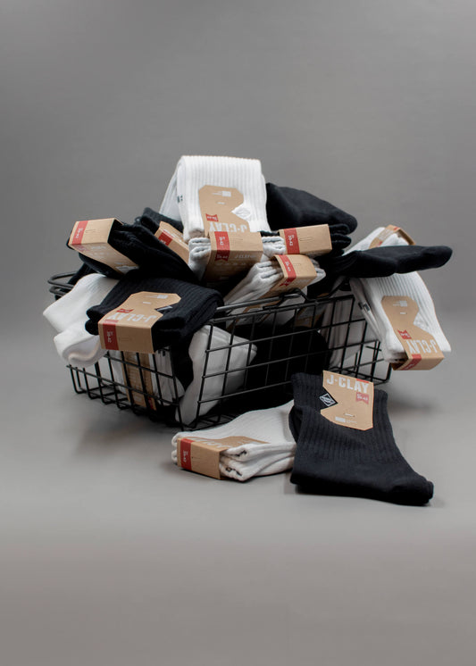 Vier J.Clay Crew-Socken - zwei schwarze, zwei weiße - mit einem kleinen gestickten geometrischen Logo in der Nähe des oberen Endes. Die Socken sind flach auf einem weißen Hintergrund in einem abwechselnden Farbmuster angeordnet. - Socken Packs für Männer