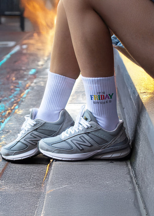 Ein Paar weiße J.Clay-Tennissocken mit gerippten Oberteilen, auf denen "ITS FRIDAY BITCHES" in fetten, bunten Buchstaben in der Nähe des Oberteils aufgestickt ist.