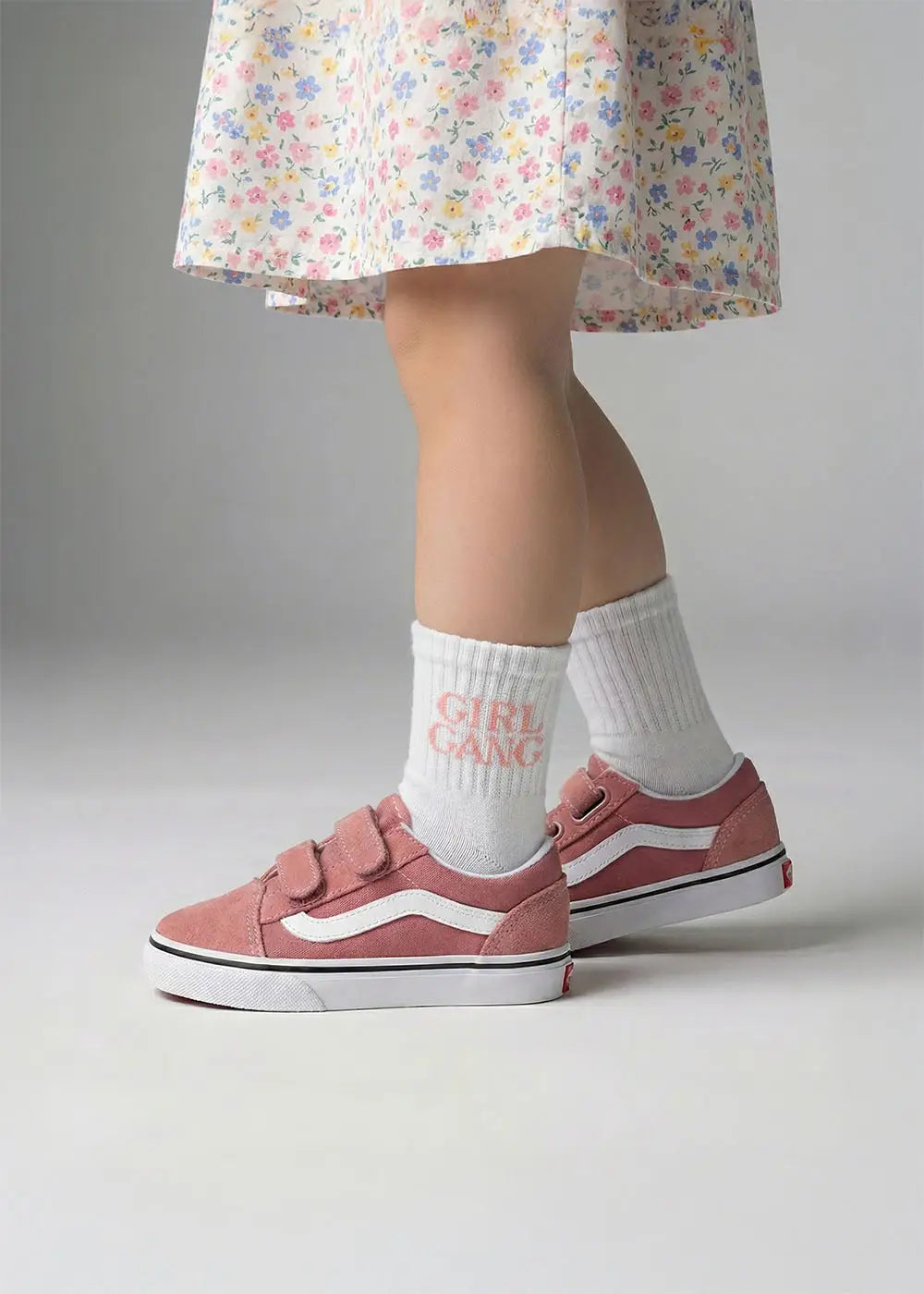 Sie trägt ein geblümtes Kleid, rosa Turnschuhe und J.Clay Girl Gang - Mini Socken.