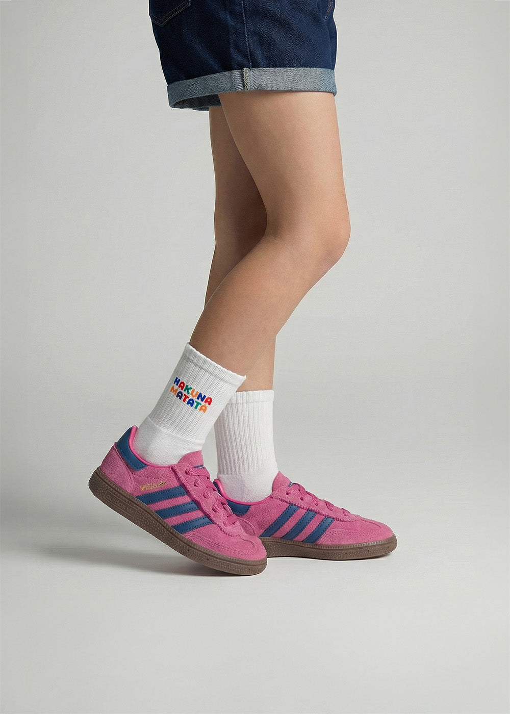 Person in rosa Turnschuhen, Jeansshorts und J.Clay Hakuna Matata - Kids Socken in Weiß.