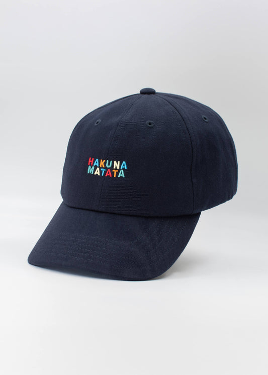 Eine marineblaue J.Clay Dad Cap mit "Hakuna Matata" in bunten Buchstaben auf der Vorderseite, die vor einem schlichten weißen Hintergrund aufgestickt ist.