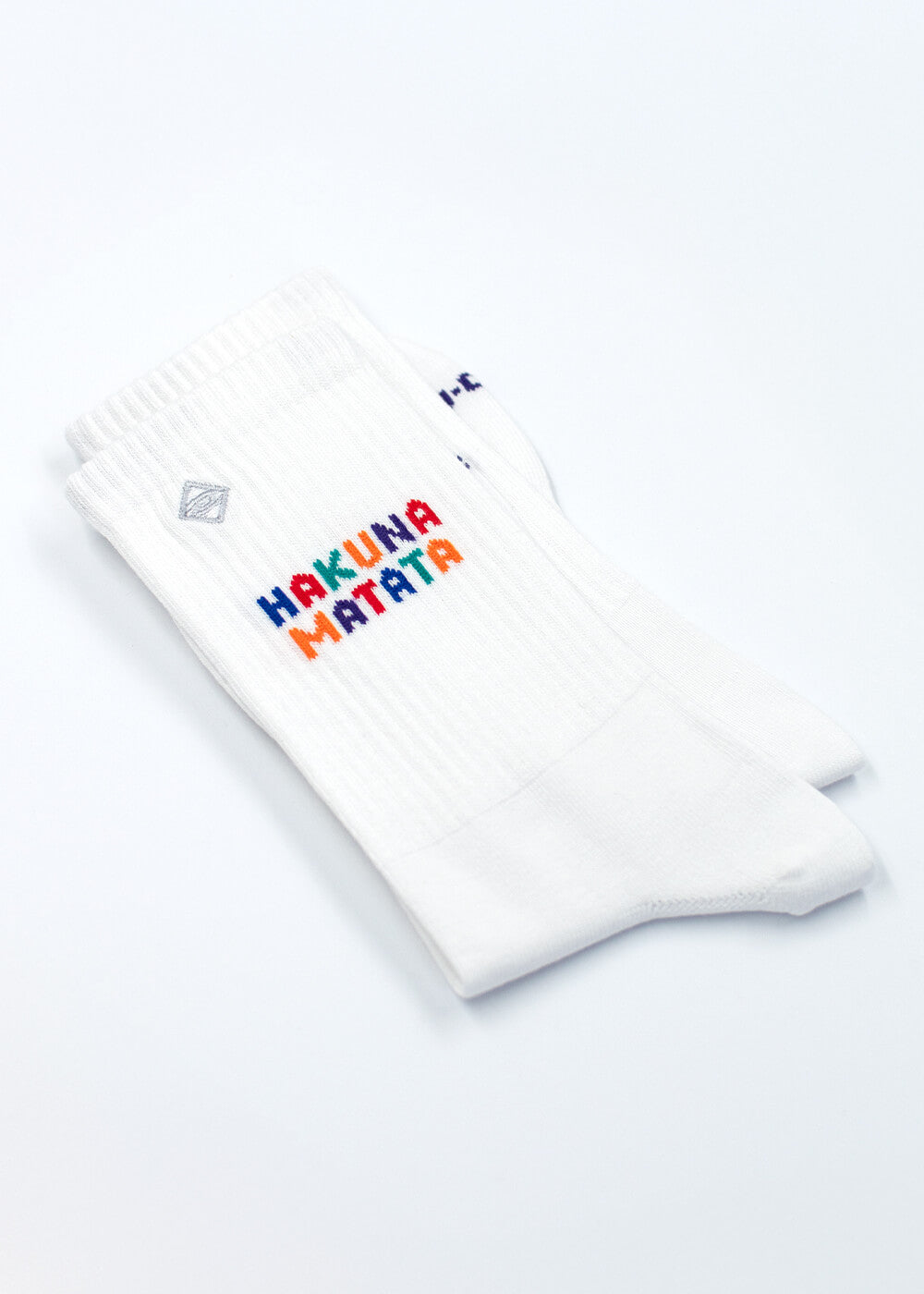 Ein Paar weiße J.Clay Tennissocken mit der Aufschrift "Hakuna Matata" in bunten, verspielten Buchstaben an der Oberseite.