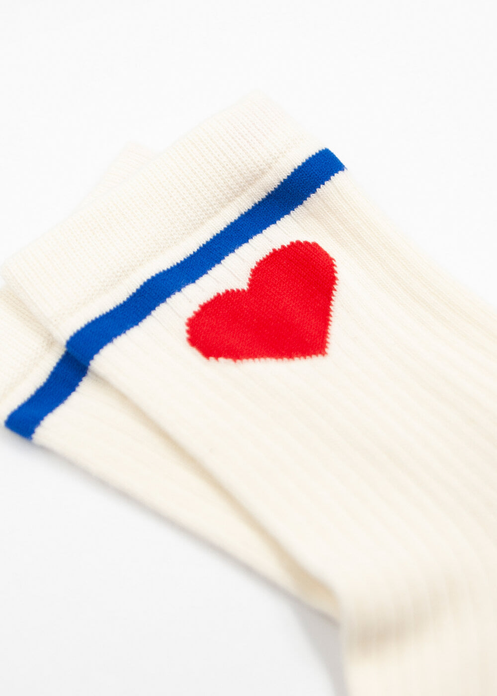Eine Nahaufnahme von J.Clay Damen Socken, weiß und gerippt mit einem blauen Streifen am oberen Ende und einem roten Herz darunter. Die Baumwollsocken Damen liegen flach auf einer weißen Unterlage.