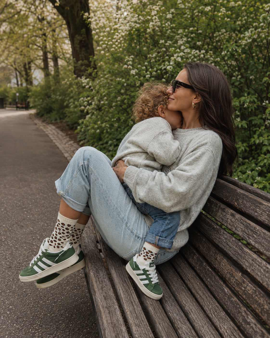 Mutter und Kind im Sternzeichen Löwe – „Fam Pack“ von J.Clay, die grüne Turnschuhe tragen und auf einer Parkbank sitzen.