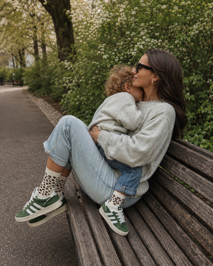 Mutter und Kind im Sternzeichen Löwe – „Fam Pack“ von J.Clay, die grüne Turnschuhe tragen und auf einer Parkbank sitzen.