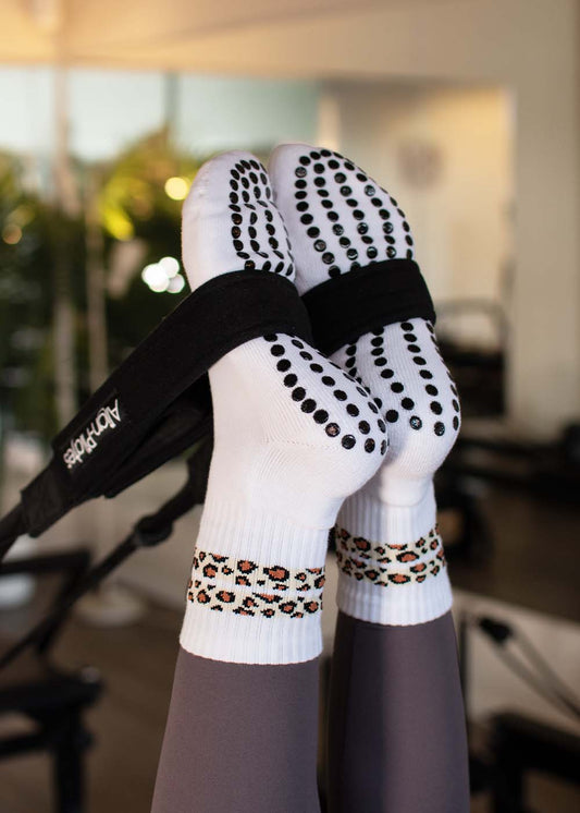 Füße in J.Clay Leo Stripes Grip Socken mit schwarzen Punkten und Leopardenmuster, auf dem Reformer Pilates Gerät.