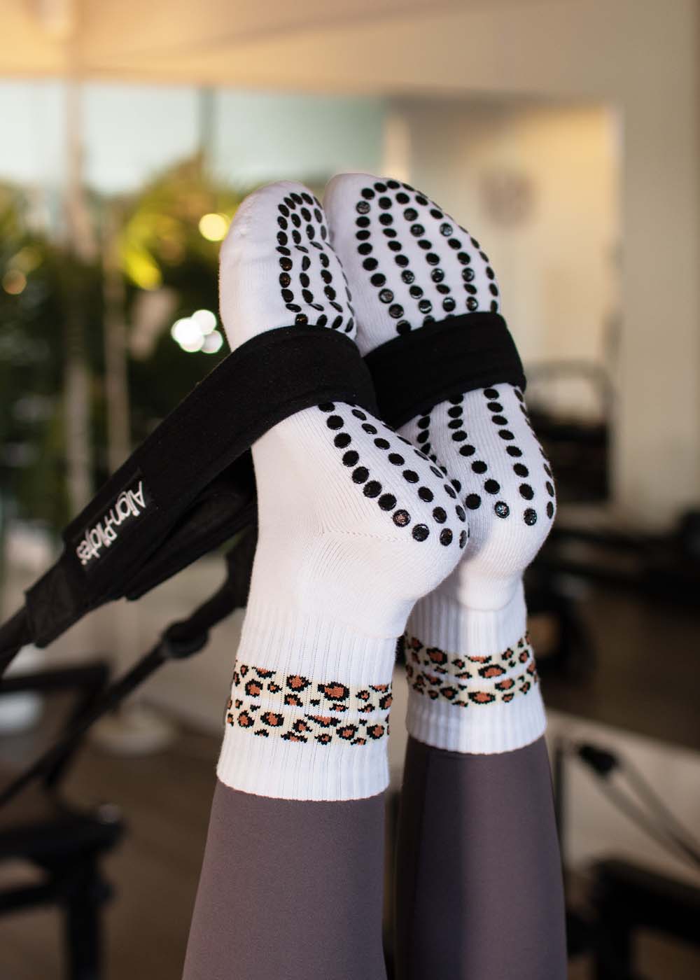 Füße in J.Clay Leo Stripes Grip Socken mit schwarzen Punkten und Leopardenmuster, auf dem Reformer Pilates Gerät.