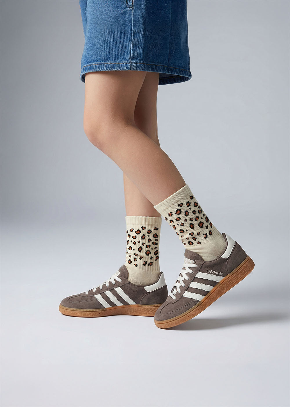 Person in Jeansshorts mit J.Clay Leo - Kids Socken und grauen Adidas-Turnschuhen mit Gummisohle.