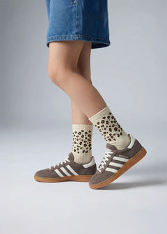 Person in Jeansshorts mit J.Clay Leo - Kids Socken und grauen Adidas-Turnschuhen mit Gummisohle.