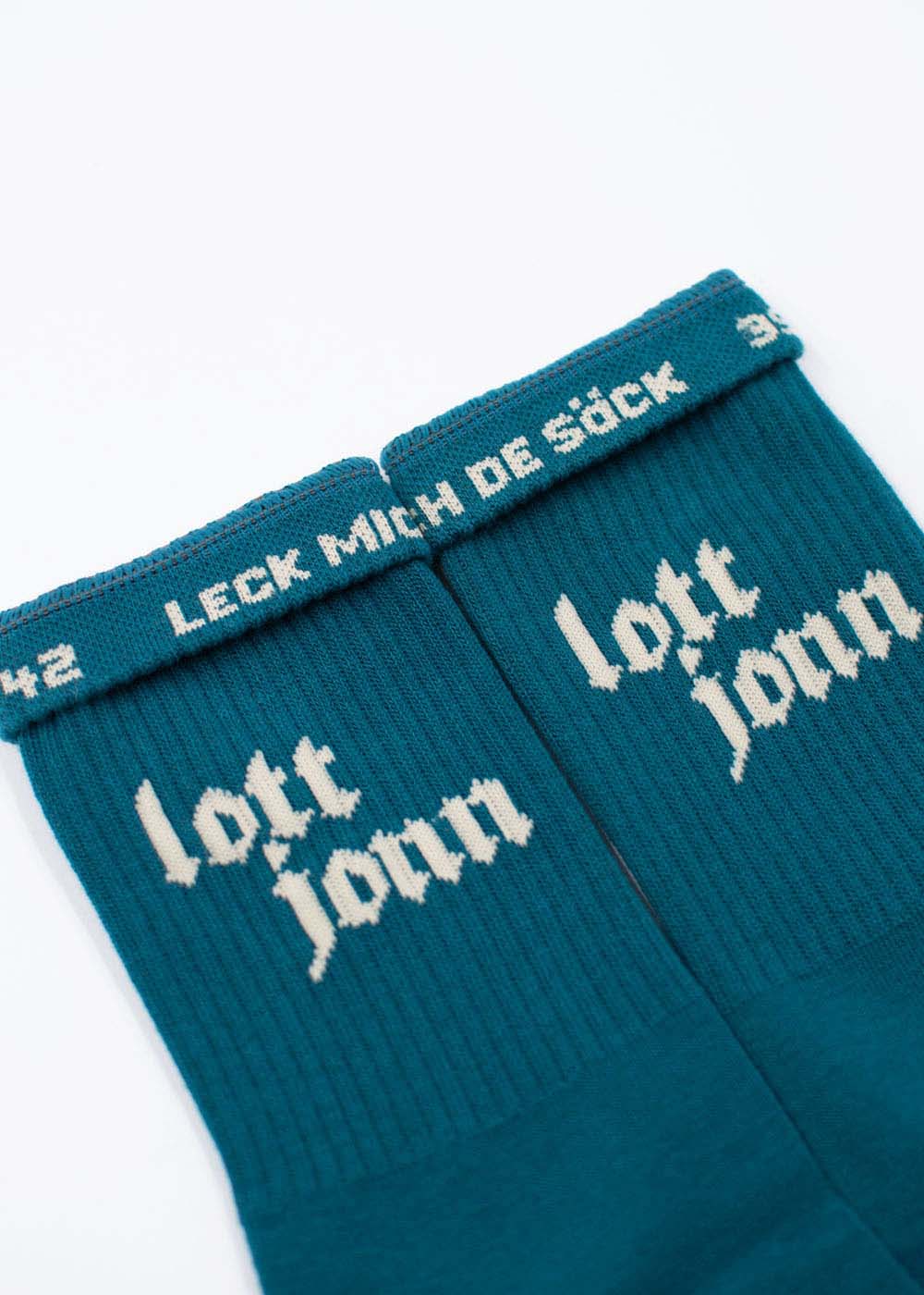 Zwei blaugrüne J.Clay Lott Jonn 2.0-Socken mit den Aufschriften „lott jonn“ und „LECK MICH DE SÖCK“ in weißer Schrift.