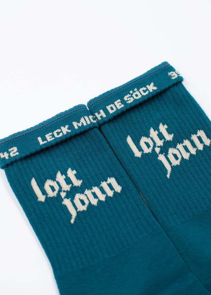 Zwei blaugrüne J.Clay Lott Jonn 2.0-Socken mit den Aufschriften „lott jonn“ und „LECK MICH DE SÖCK“ in weißer Schrift.