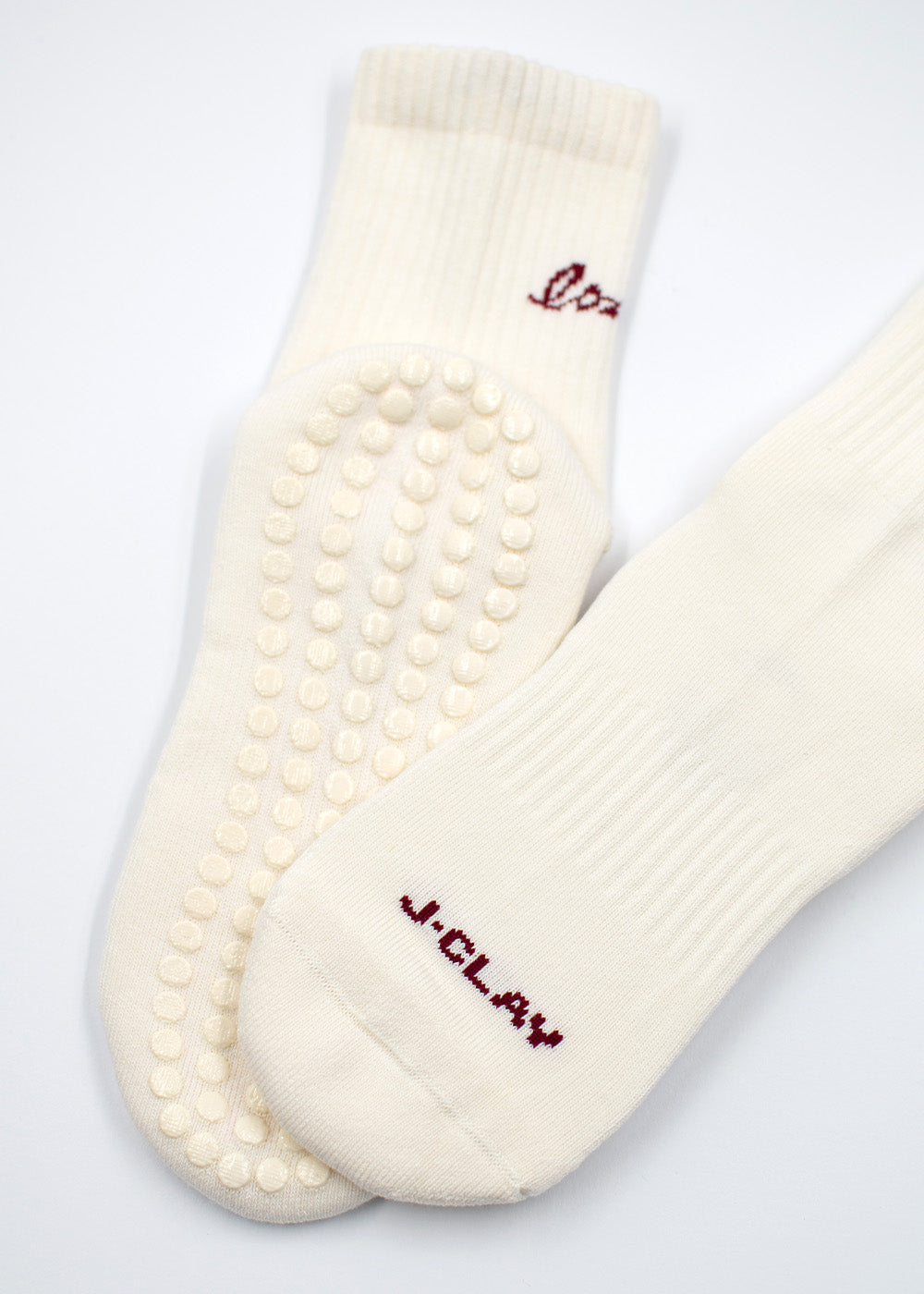 Zwei weiße J.Clay Love Grip Socken mit Eco Grip Sohlen und rotem J.Clay Text auf einem.
