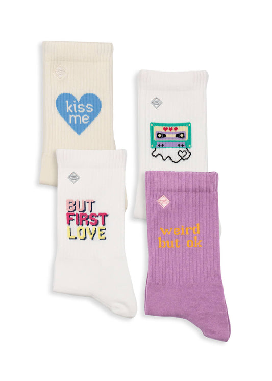 J.Clay bietet vier Paar Tennissocken mit einzigartigen Designs an: ein blaues Herz mit "kiss me", ein Kassettengespenst, "BUT FIRST LOVE" in bunten Buchstaben und "weird but ok" in gelb auf lavendel.
