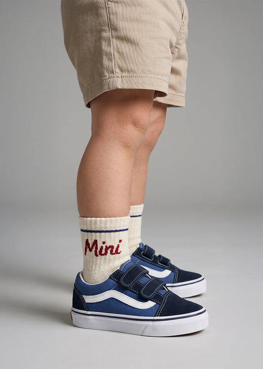 Kind in khakifarbenen Shorts, marineblauen Turnschuhen und J.Clay Mini-Socken mit roter Aufschrift "Mini".