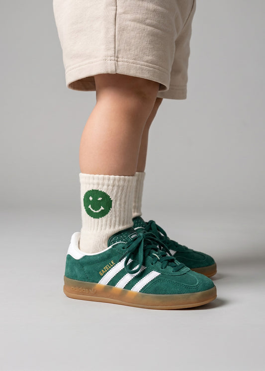 Kind in grünen Adidas-Schuhen, beigen J.Clay Smiley-Socken mit grünem Smiley – kleines grünes Smiley-Gesicht.