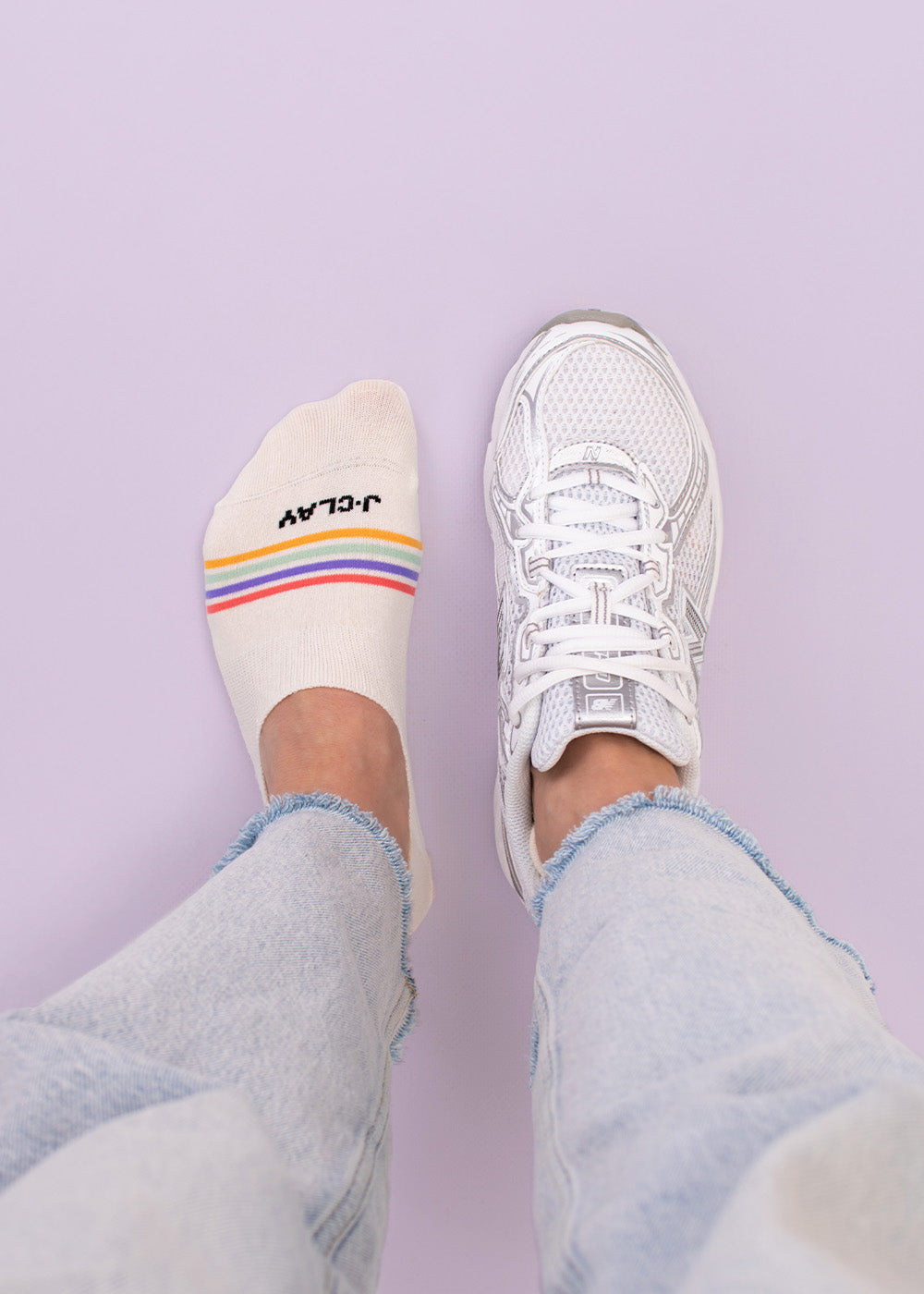 Person in hellen Jeans, ein Fuß in Sneaker Socken, der andere in J.Clay Multi Stripes Füßlinge.