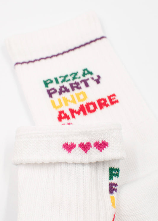 J.Clay white Kindersocken ab 5 Jahren mit buntem PIZZA PARTY UND AMORE Text und kleinen pinken Herzen am Bund. Eine Kinder Tennissocke ist umkrempelt, um die süßen Herzchen zu zeigen.