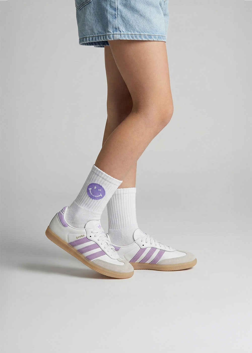 Person in Jeansshorts, die J.Clay Purple Smile - Kids Socken und lila gestreifte Turnschuhe trägt.