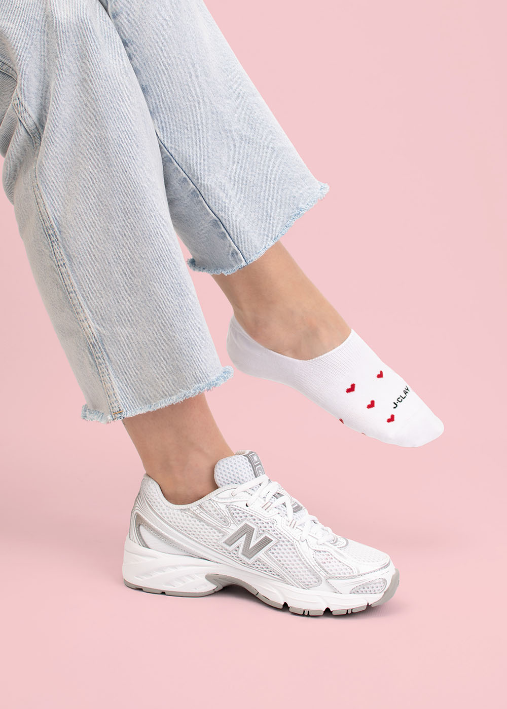 Person in hellen Jeans, weißen Turnschuhen und J.Clay Red Hearts Füßlinge mit Herzmuster.