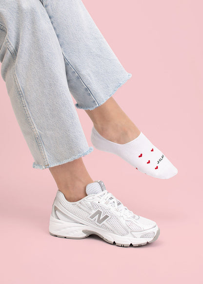 Person in hellen Jeans, weißen Turnschuhen und J.Clay Red Hearts Füßlinge mit Herzmuster.