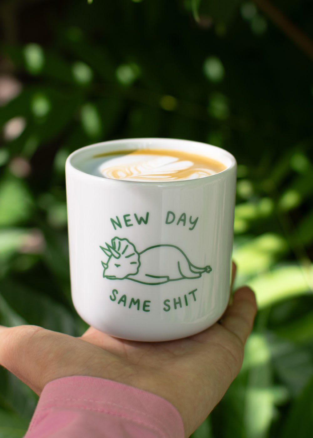 J.Clay New Day – Tasse: weiße Kaffeetasse mit Dinosaurier, Latte-Art und dem Schriftzug „NEW DAY SAME SHIT“.