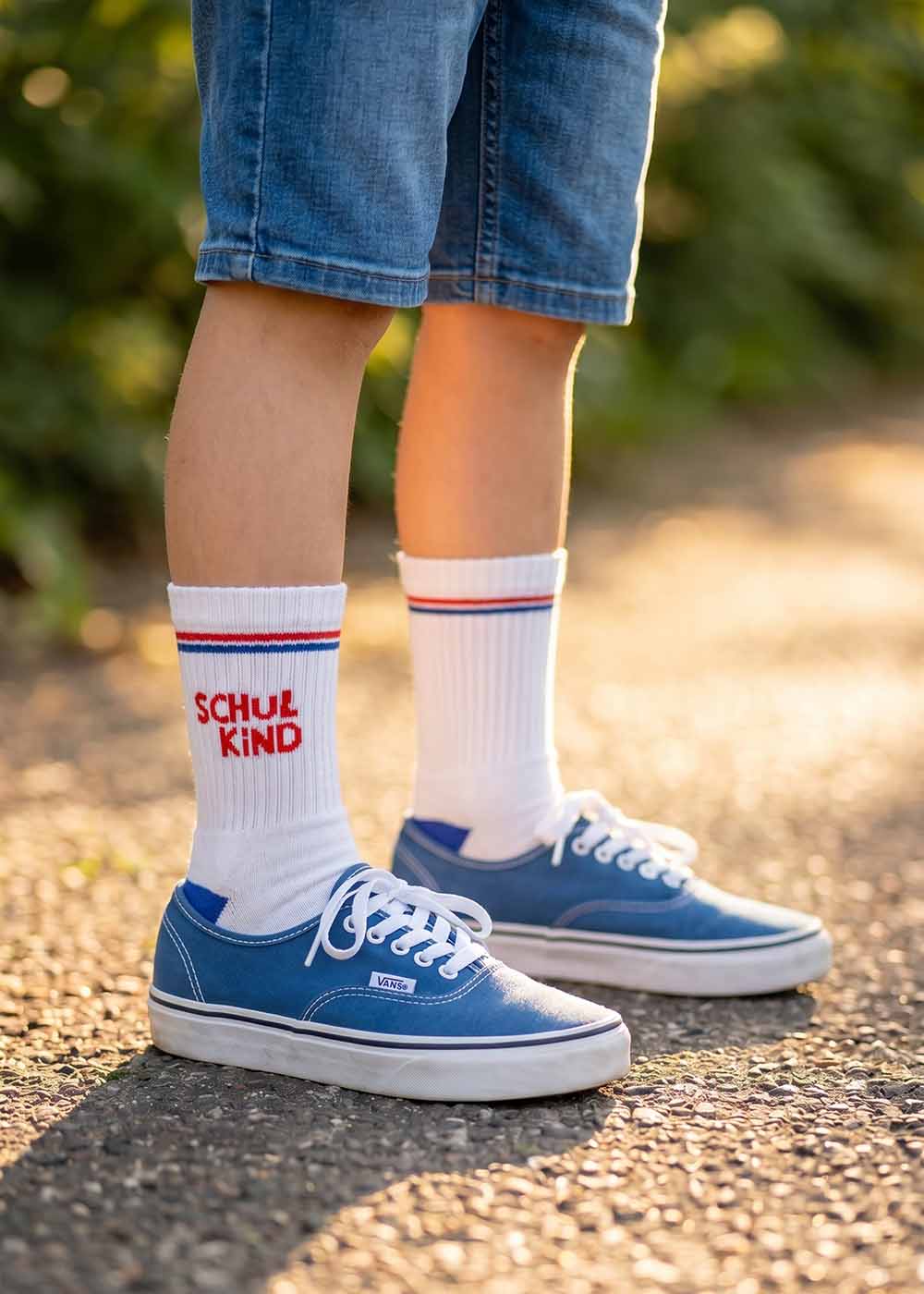 Kind in J.Clay Schulkind - Red Blue Kids Turnschuhen, Jeansshorts und weißen Socken.