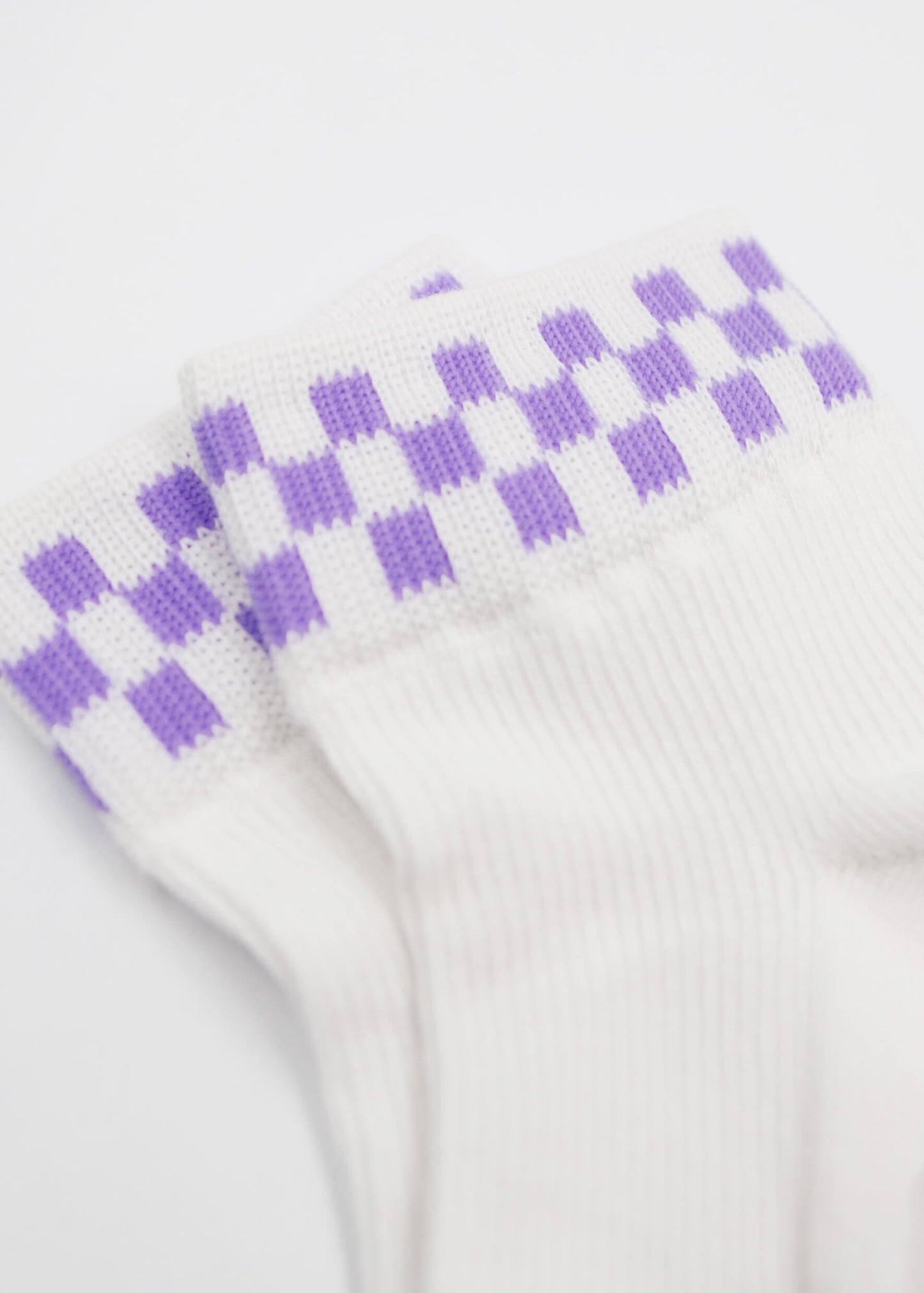 Eine Nahaufnahme der J.Clay Grape Check Sneaker Socken Damen zeigt ein lilafarbenes Karomuster in der Nähe der Bündchen vor einem schlichten weißen Hintergrund.