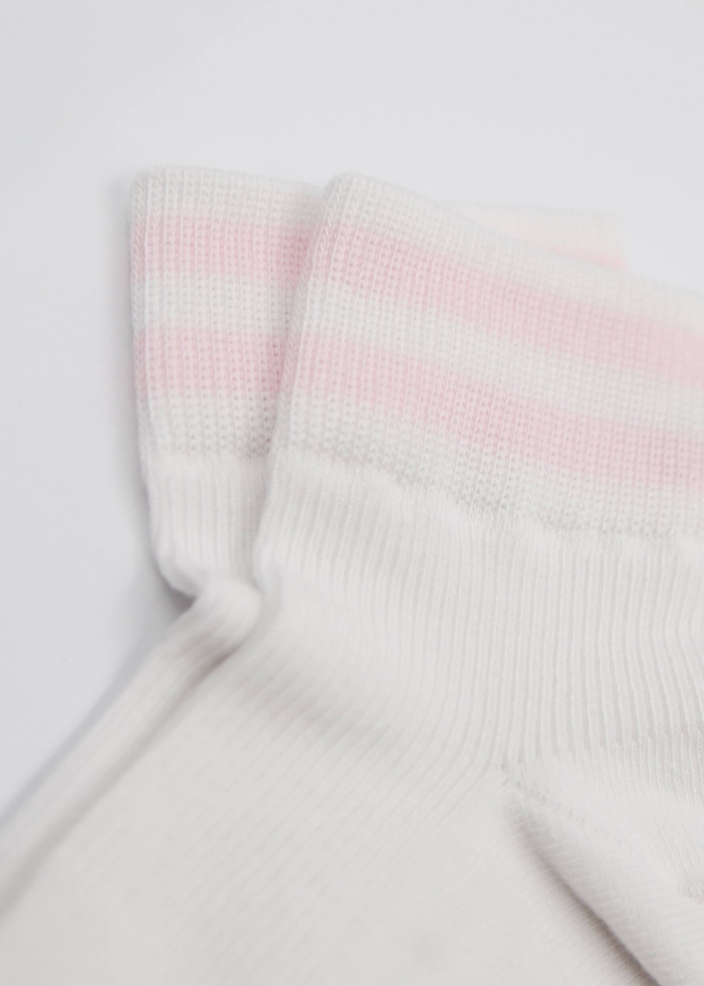 Nahaufnahme von zwei J.Clay Sneaker Socken aus atmungsaktivem Material, mit rosafarbenen und weißen Streifen an den Bündchen, arrangiert auf einer hellen Oberfläche.