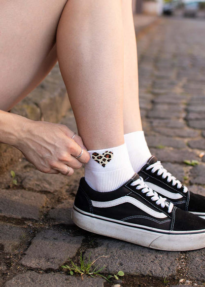 Person in Vans trägt weiße J.Clay Leo Heart – SSH-Socken mit einem kleinen Herz im Leopardenmuster.